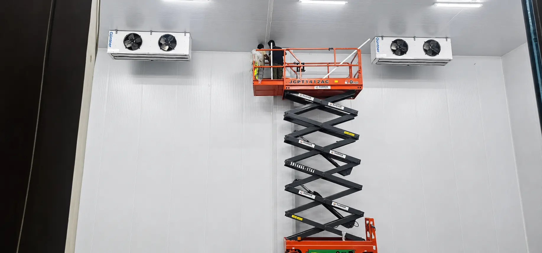 Evaporator Install: Technicians on elevated scissor lift installing industrial ceiling-mounted evaporator coils in cold storage warehouse