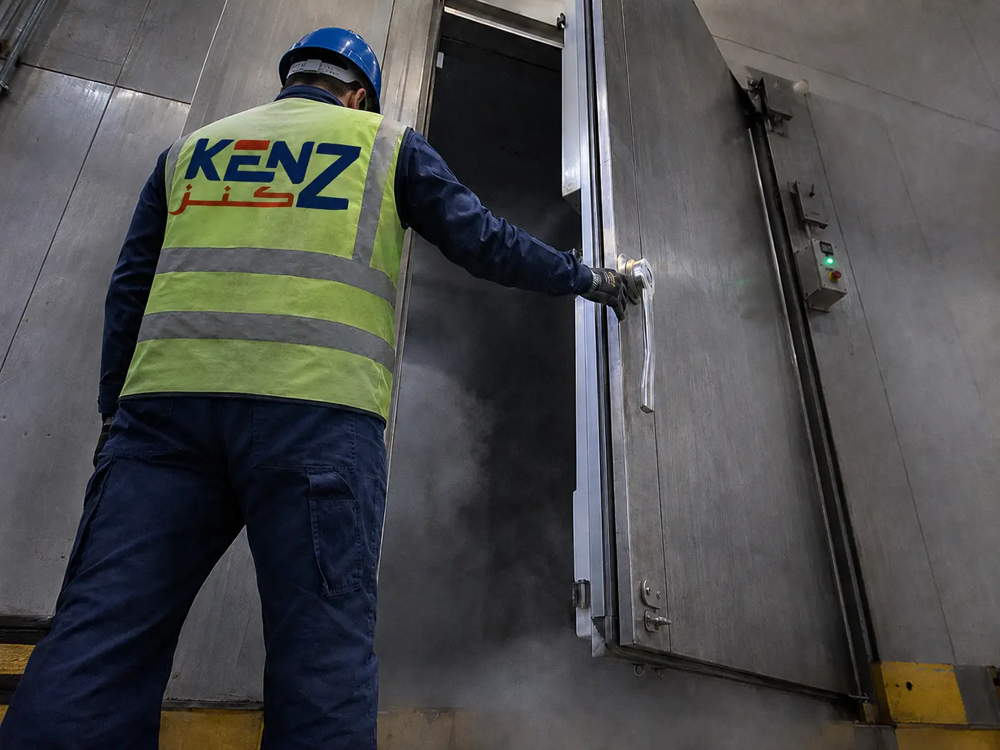 Industrial Walk-In Freezers: Kenz Cold technician opening heavy industrial door with cold vapor escaping in Saudi Arabia