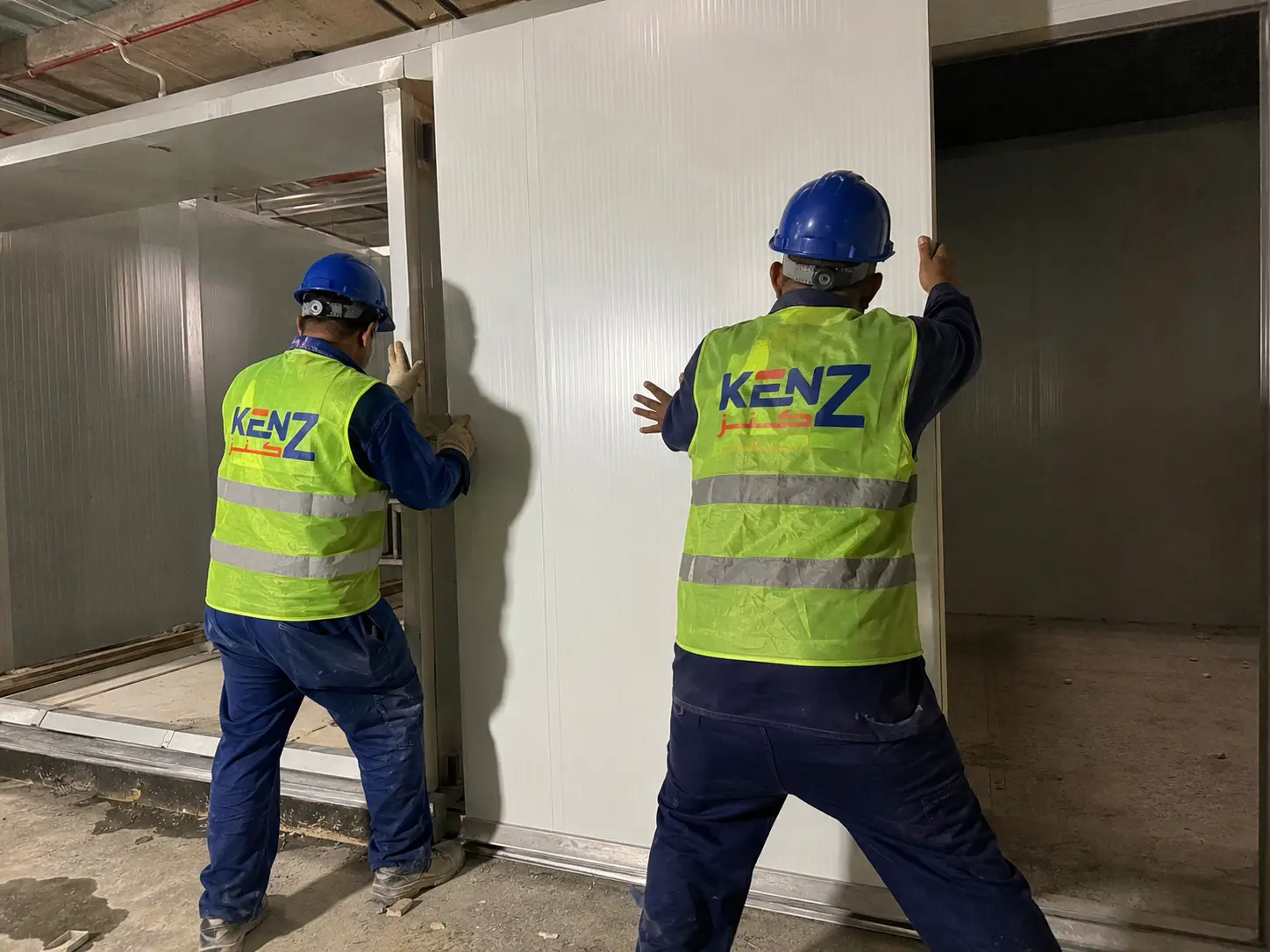 Wall Assembly: Contractors manually fitting thick PU insulated wall panels for commercial cold room