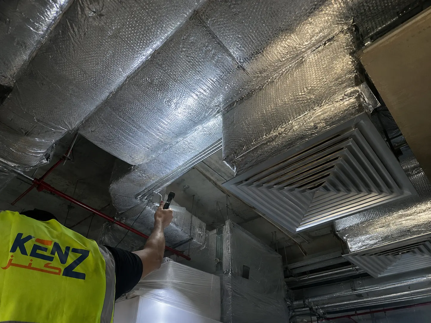 Technician using flashlight to inspect insulated ceiling HVAC ducts and diffusers
