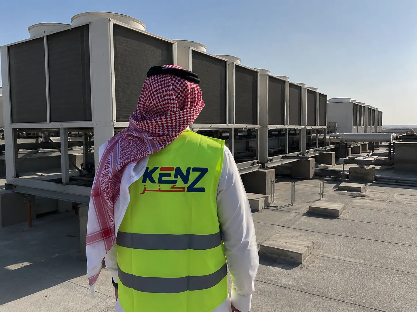 Saudi Project Manager inspecting massive industrial air-cooled HVAC chillers on a commercial roof
