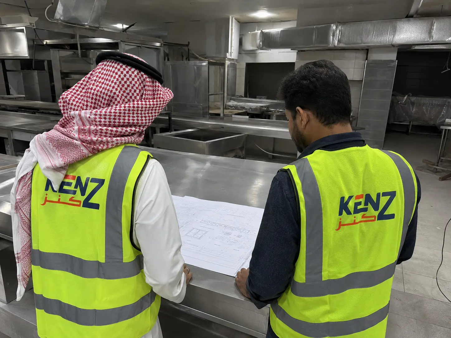 Kenz engineering team reviewing kitchen workflow blueprints on stainless steel prep table
