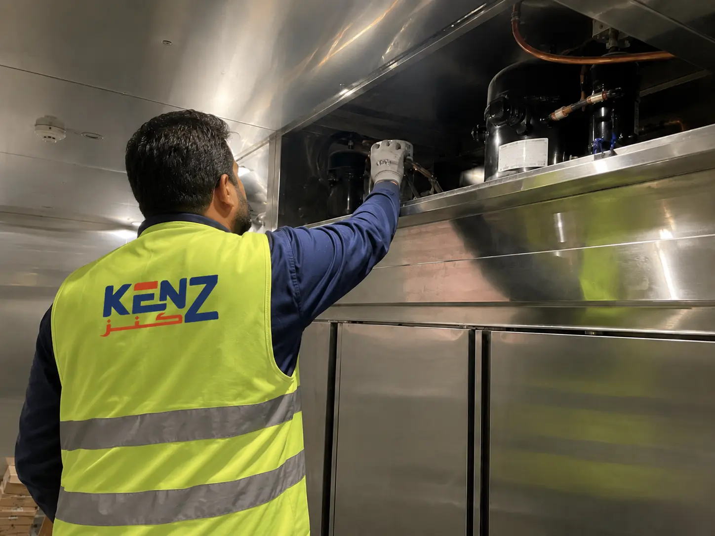 Worker inspecting refrigeration compressor unit in commercial kitchen