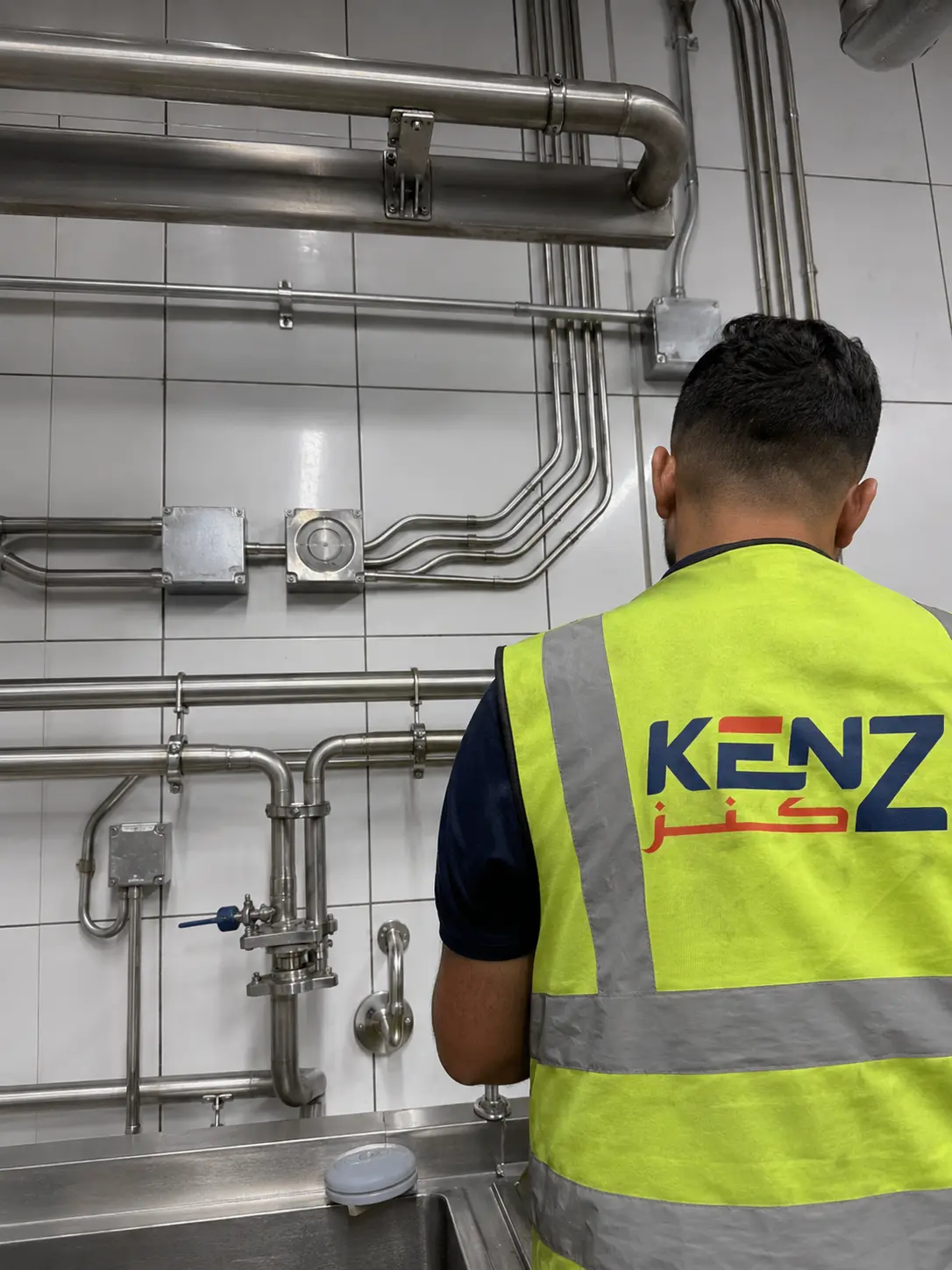 Stainless steel sanitary plumbing and electrical conduits on kitchen wall