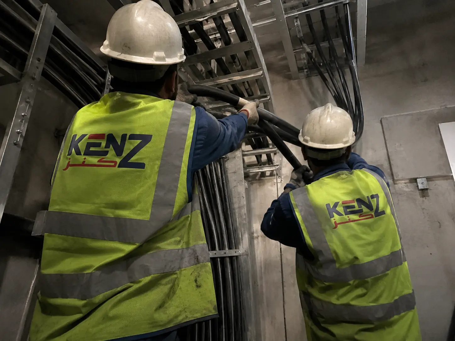 Kenz technicians pulling thick high-voltage electrical cables along overhead steel cable tray