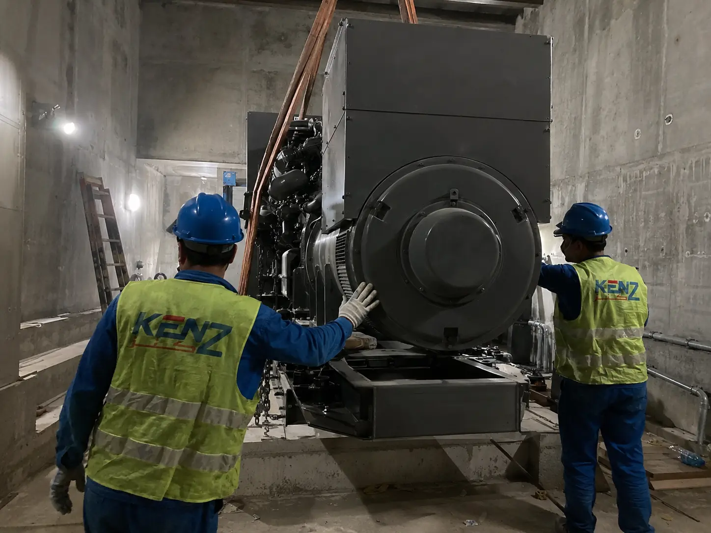 Kenz workers guiding massive industrial diesel generator being lowered into concrete power room
