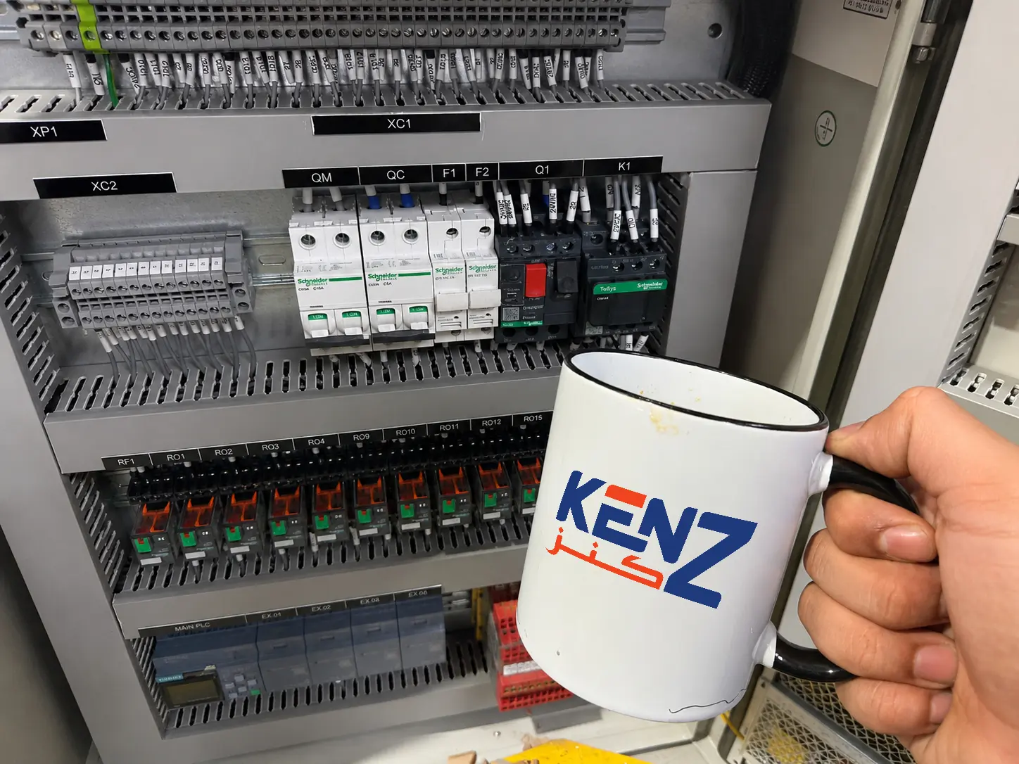 Kenz Contracting branded mug in front of newly installed commercial electrical panel