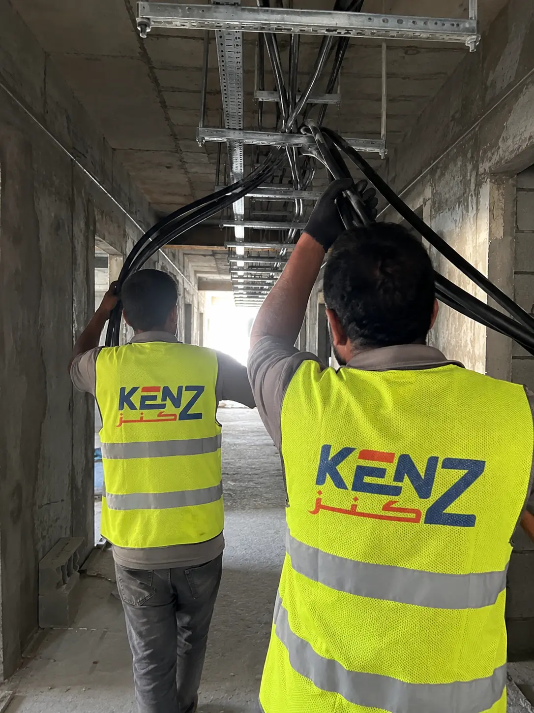 Electrical workers pulling thick cables through overhead commercial cable trays