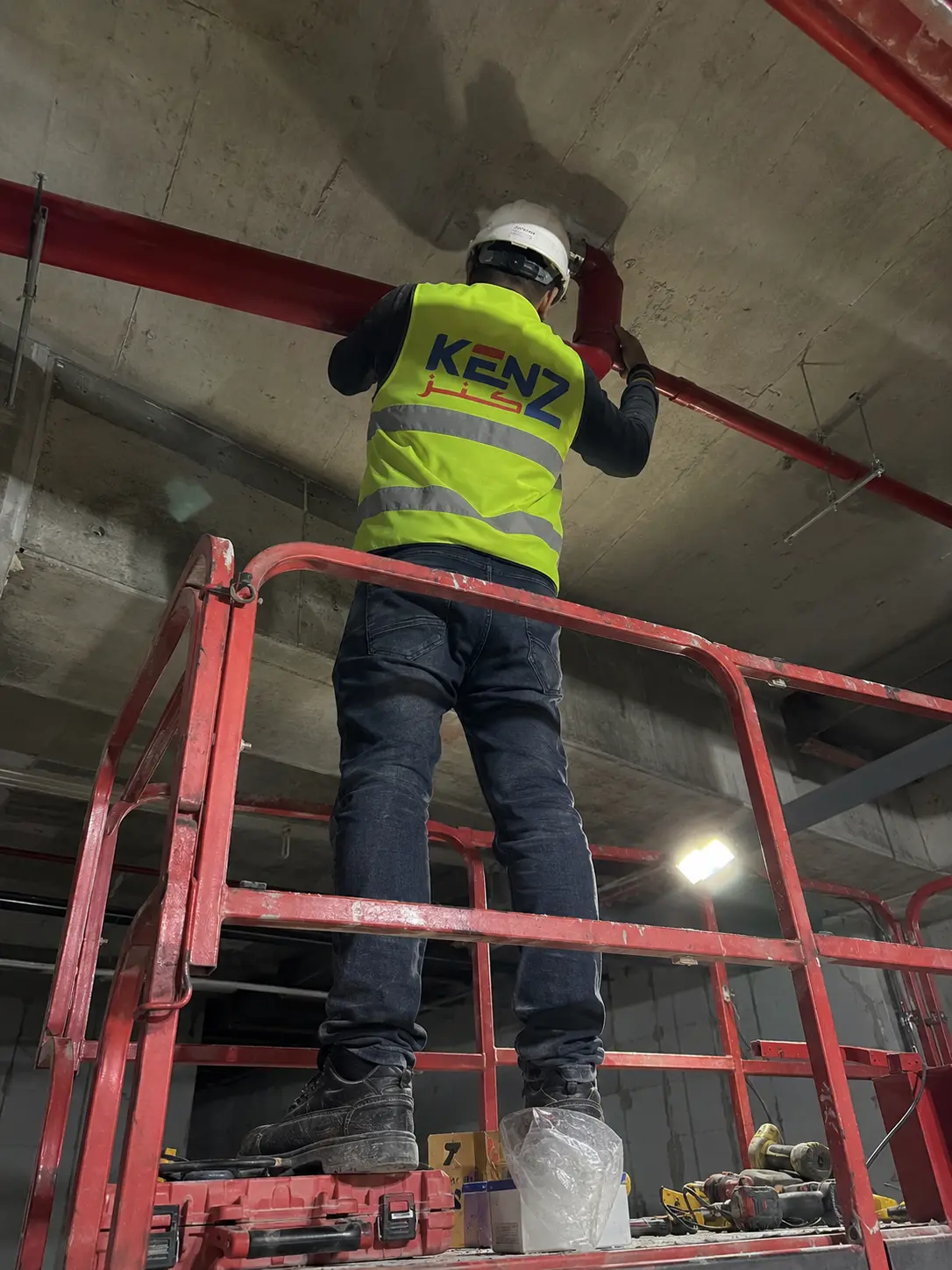 Fire protection technician on scissor lift installing red ceiling sprinkler pipes