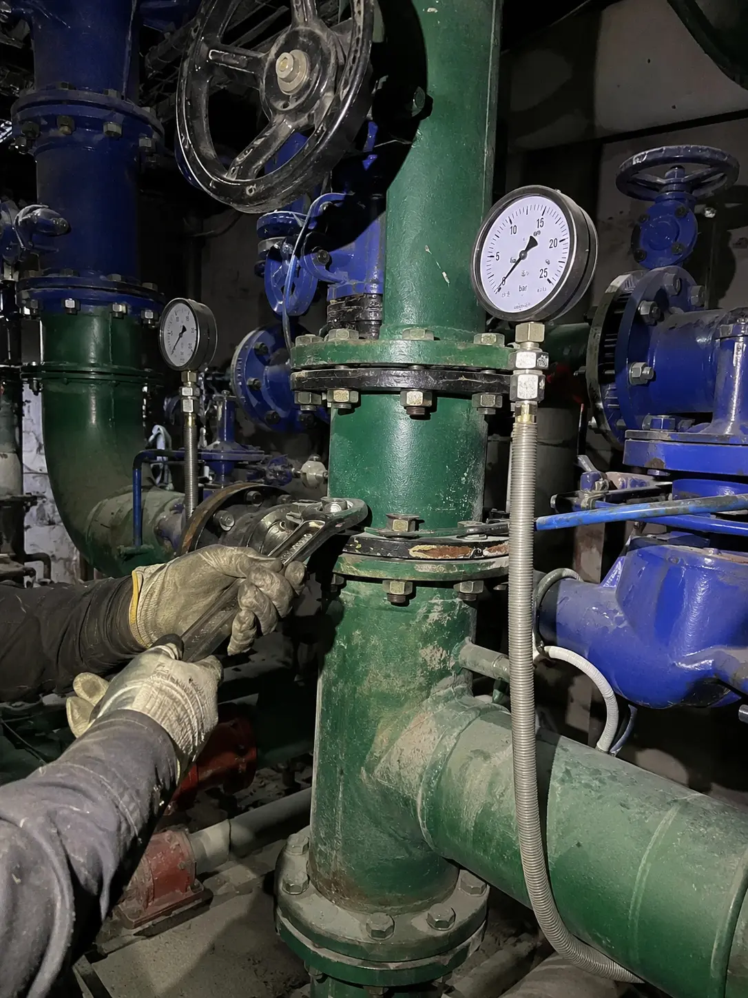 Plumbing technician wrenching heavy industrial green water pipes