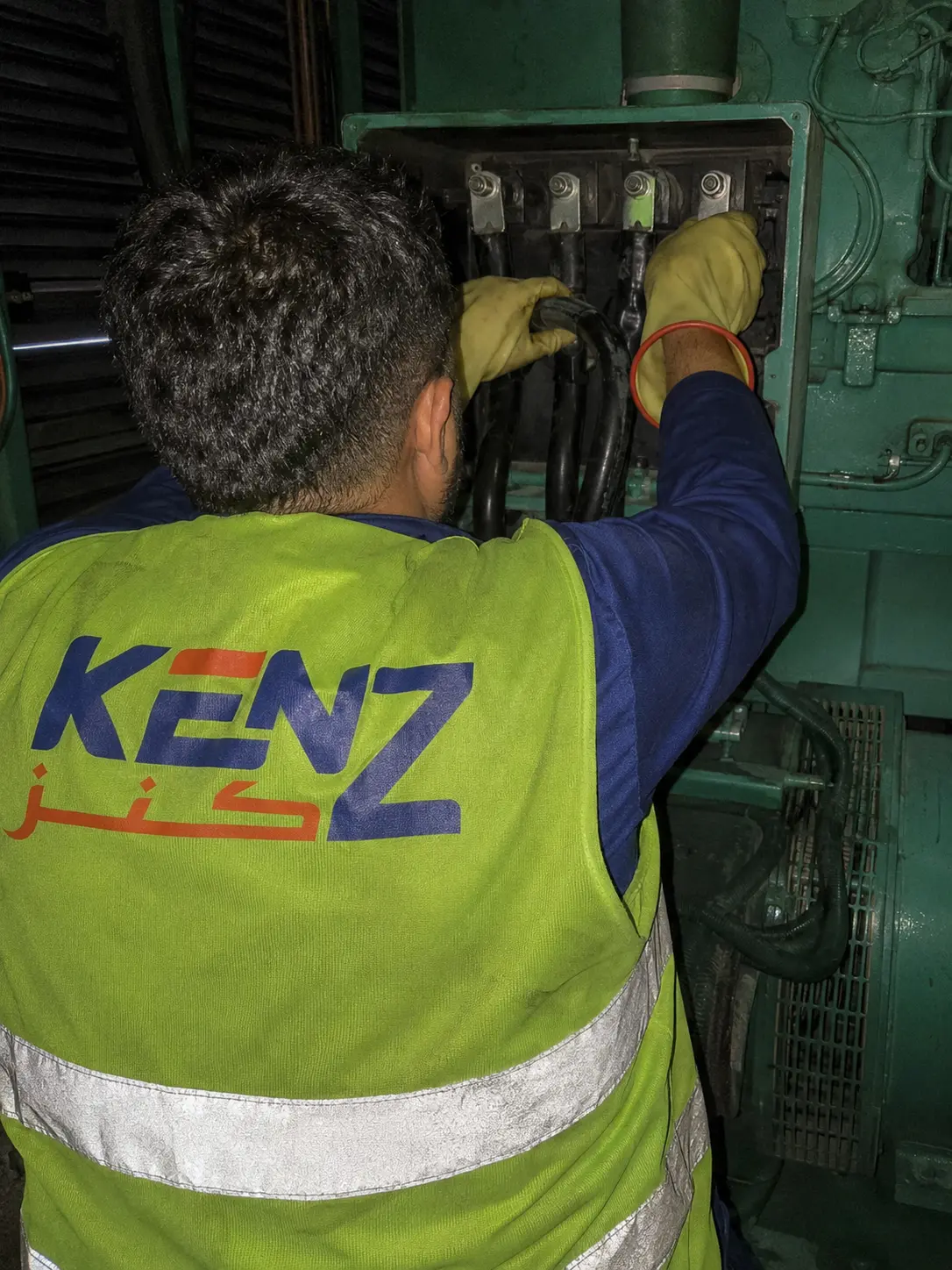 Technician connecting heavy black power cables inside industrial generator control panel